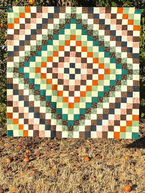 A trip around the world quilt is hanging in front of a big pear tree.