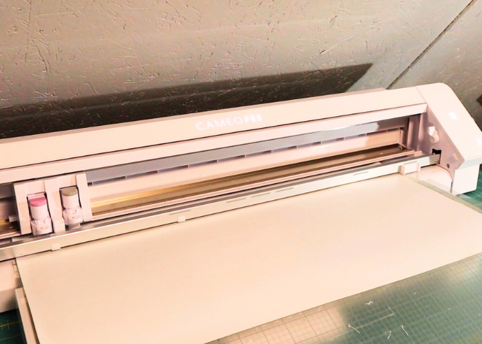A step-by-step demonstration of cutting HTV on a Silhouette Cameo machine. The blade is precisely cutting a popsicle holder design on the HTV sheet.