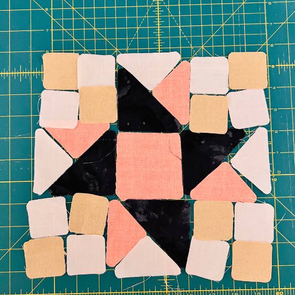 Hands piecing together fabric squares to create the quilt block design