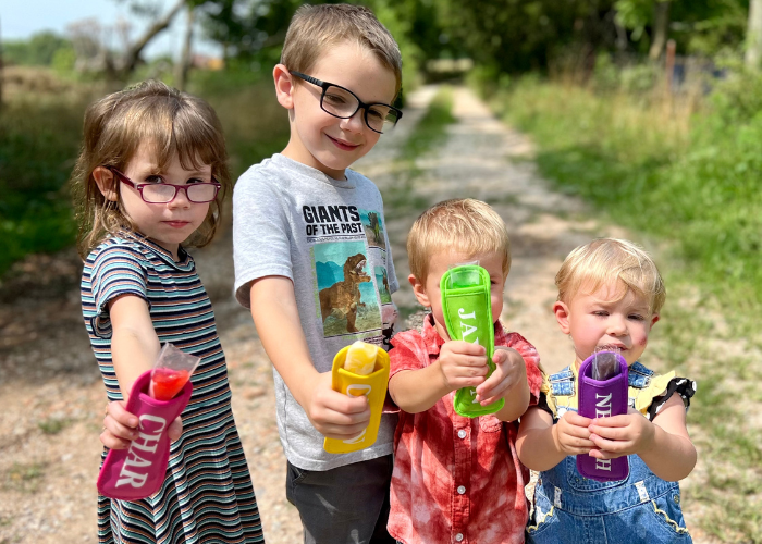 Kids eagerly pressing their HTV-decorated popsicle holders onto their popsicle, showing off their customized design featuring their names.