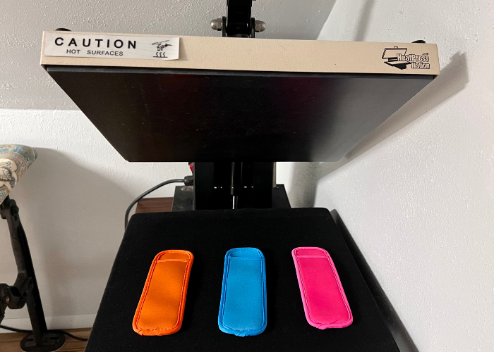 A heat press machine in action, applying the HTV design onto three popsicle holders. The even pressure ensures a smooth and durable transfer of the design to the holder.