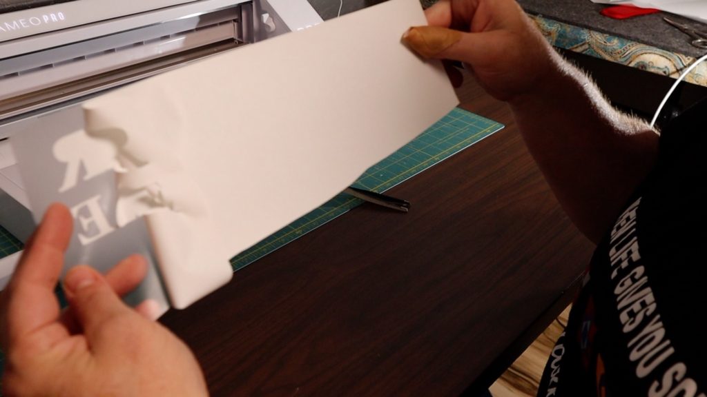 A crafty hand using tweezers to weed the excess HTV from a popsicle holder design, revealing a beautifully customized popsicle holder with a cool name pattern.