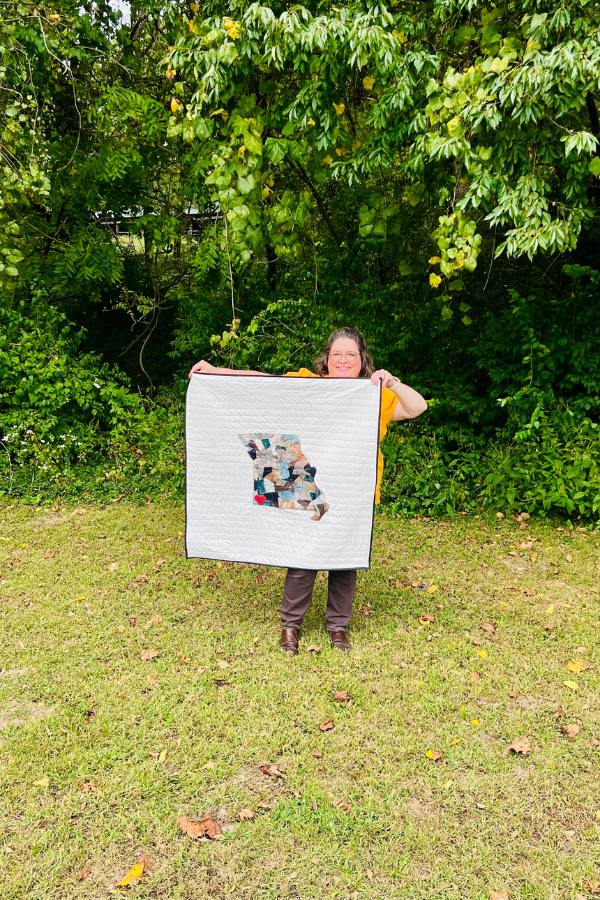 Holding a quilted wall hanging with a collaged state outline.